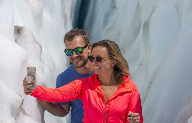 A couple in their mid-thirties take a selfie snap while touring Franz Josef Glacier